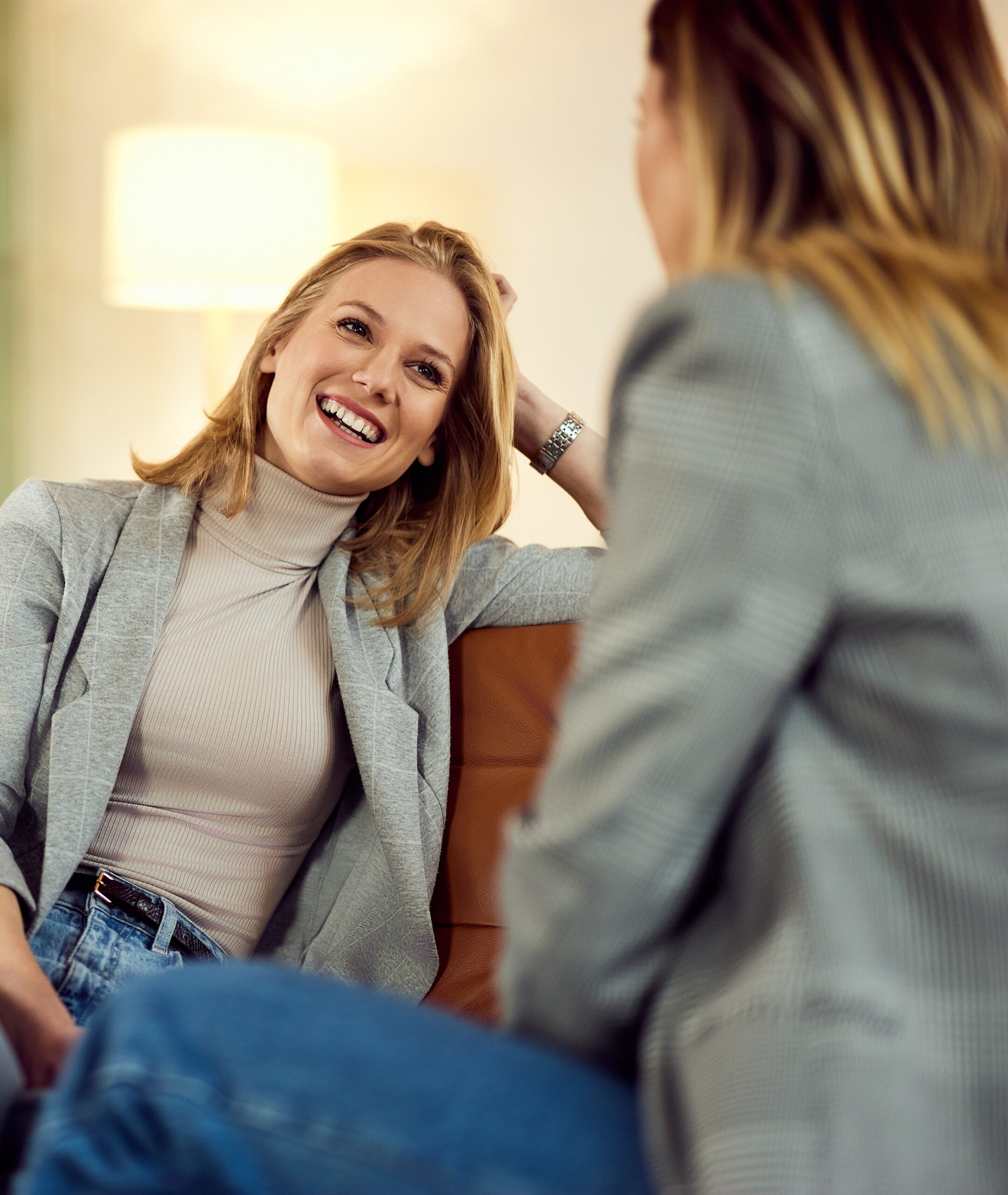Two smiling female friends chatting over tea while relaxing indoors