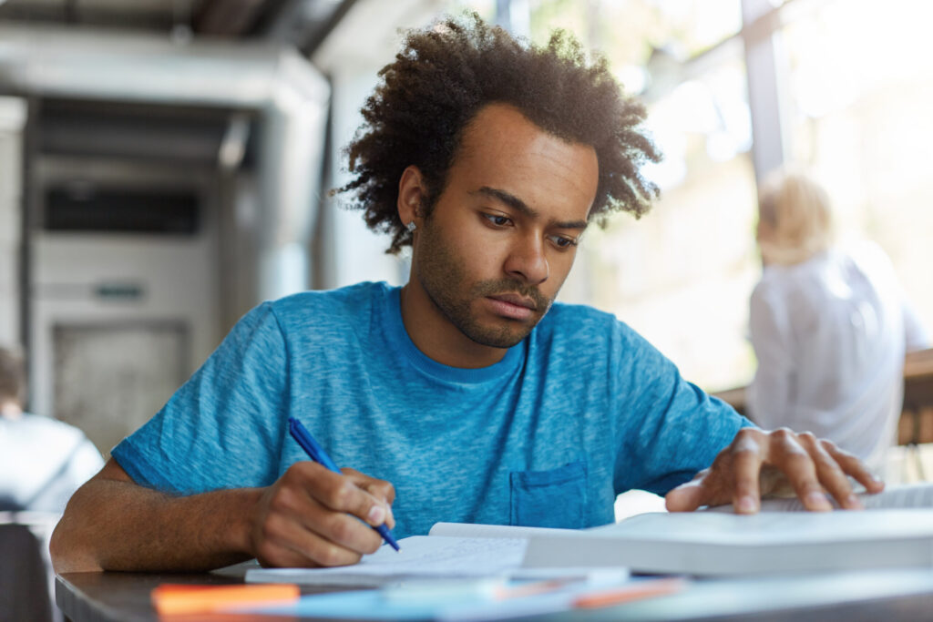 Focused young male student in a blue t-shirt reading and studying in a bright room